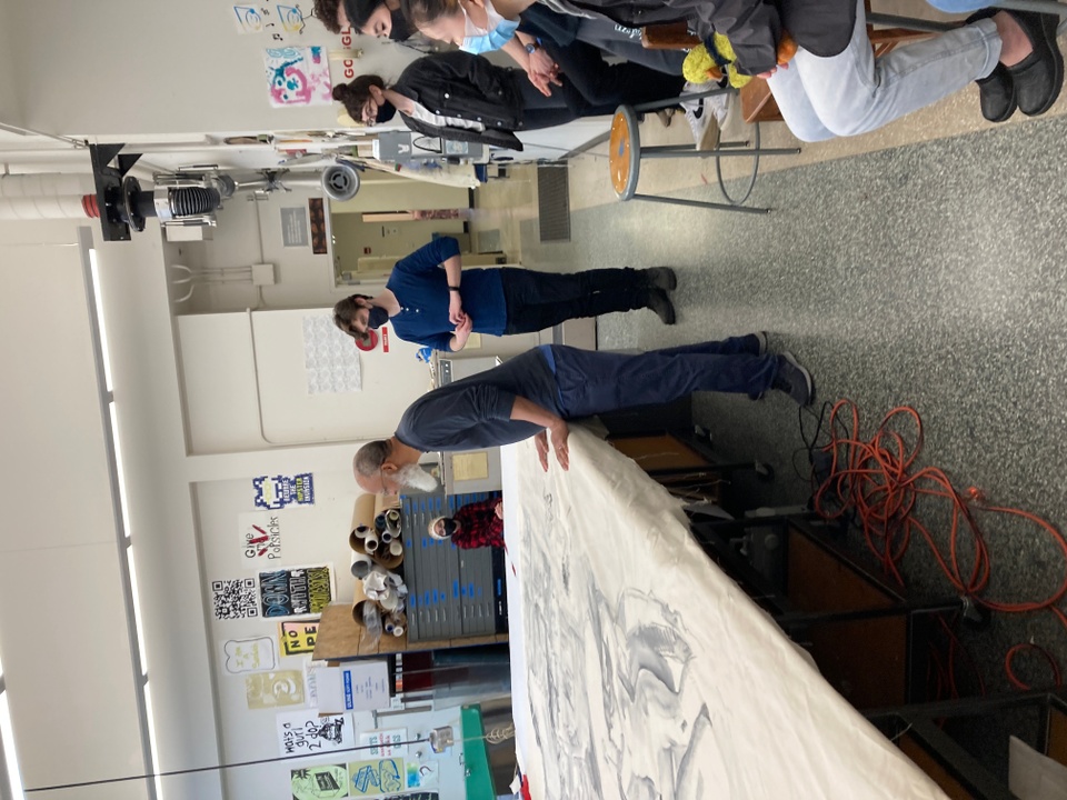 Group of students watching as artist looks at print on large canvas on a table
