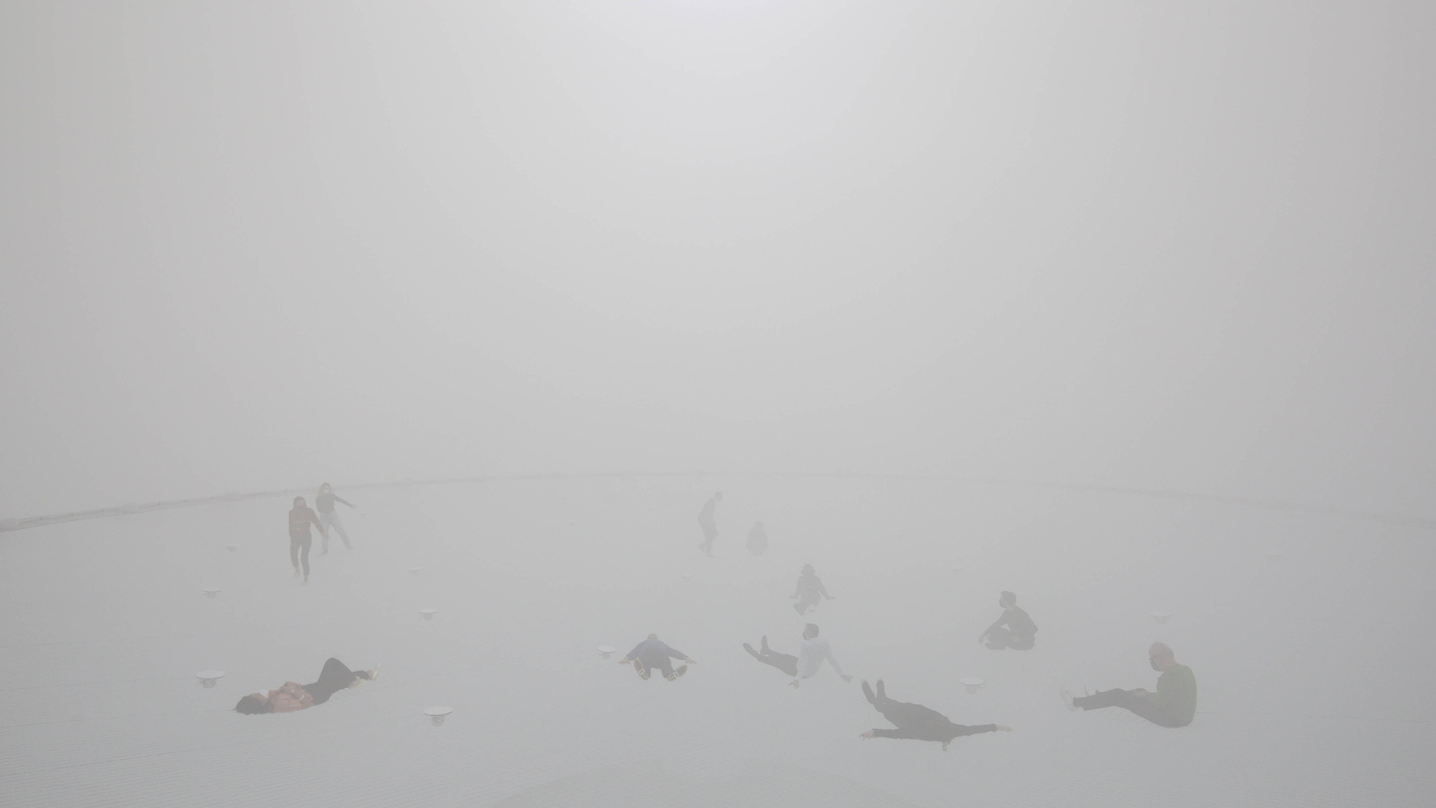 People recline on a vast net in a foggy, white environment where the edges of space dissolve in the atmosphere