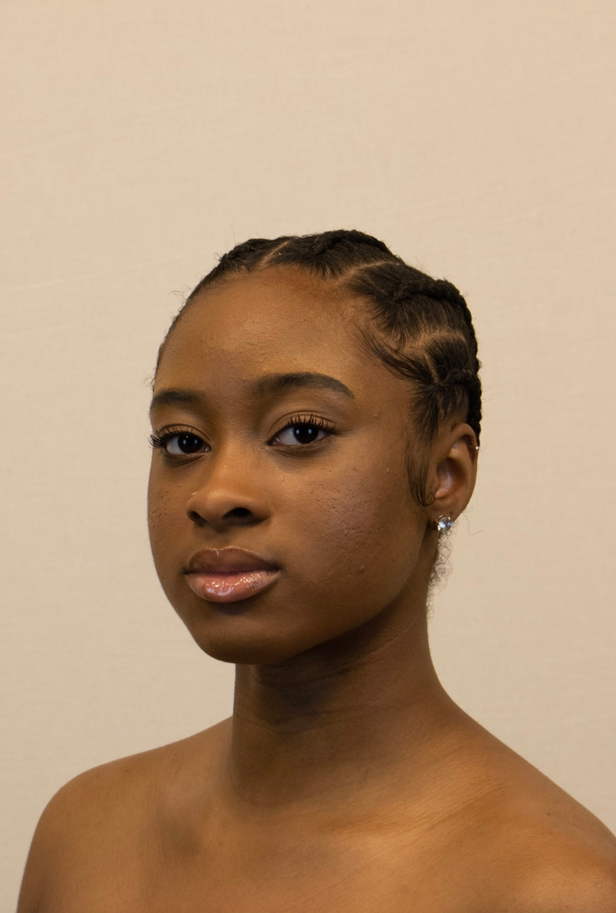 A headshot of dancer Kai Irby, a Black woman who is seen from the shoulders up looking directly at us at a slight angle. She smiles slightly and had her hair braided in rows. 