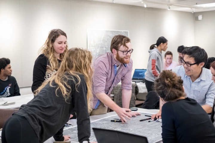 Several people leaning over a city plan on a table and talking animatedly.