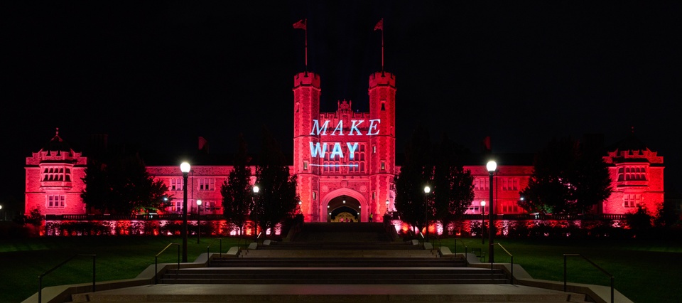 Brookings Hall at night, lit up with red uplights and projected text reading "Make Way."