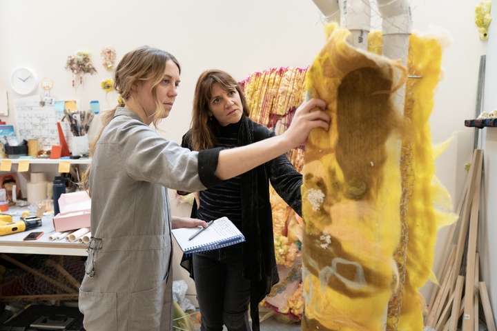A student shows a bright yellow artwork to Dana Levy in studio.