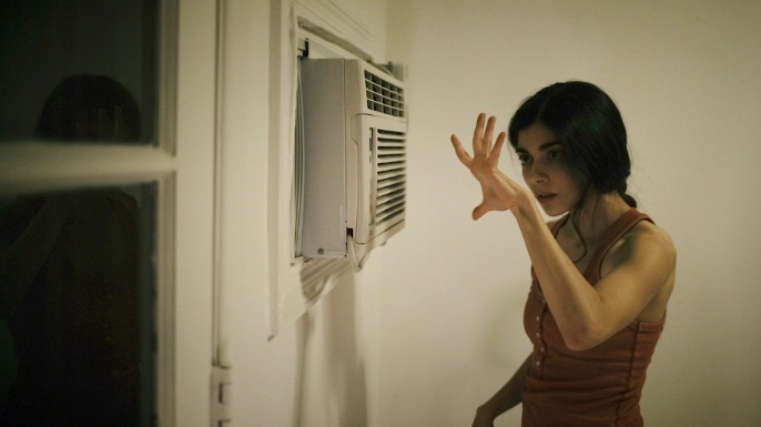 A dancer holds up her hand looking at a window air conditioner unit