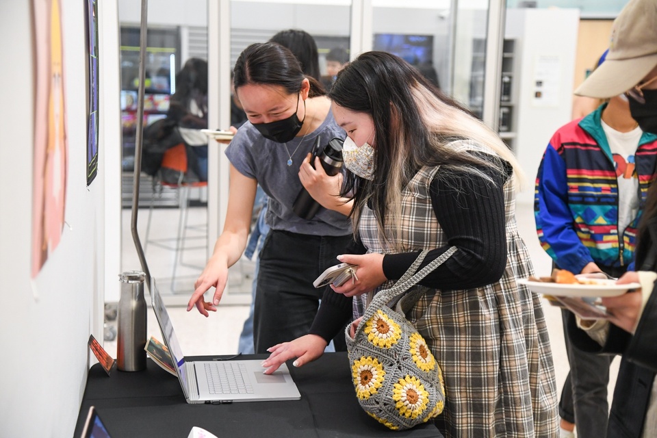 Two students click through a laptop to peruse Technomancy Tactics