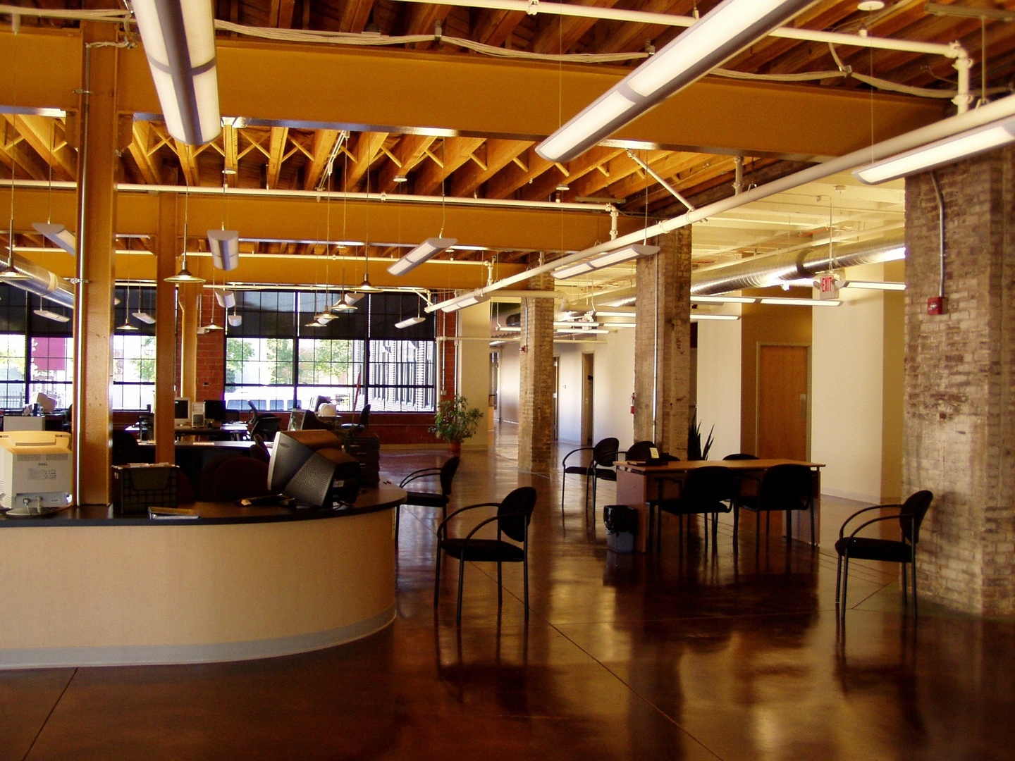 Interior view of renovated office space showing exposed timber structure and masonry columns with suspended lights