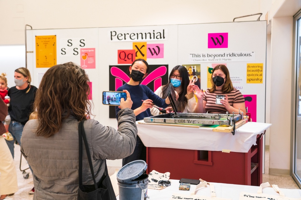 Students operating a screenprinting station pose for someone taking their photo with a phone.