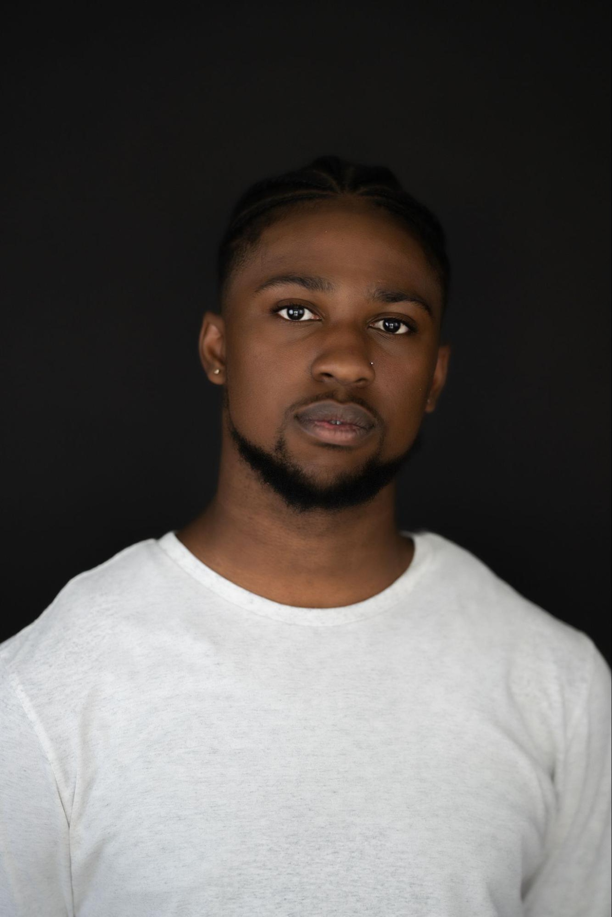 A headshot of dancer Destin Morisset, a Black man with short hair, a thin mustache, and a beard along his jaw line. He looks intently at us, wearing a white t-shirt. 