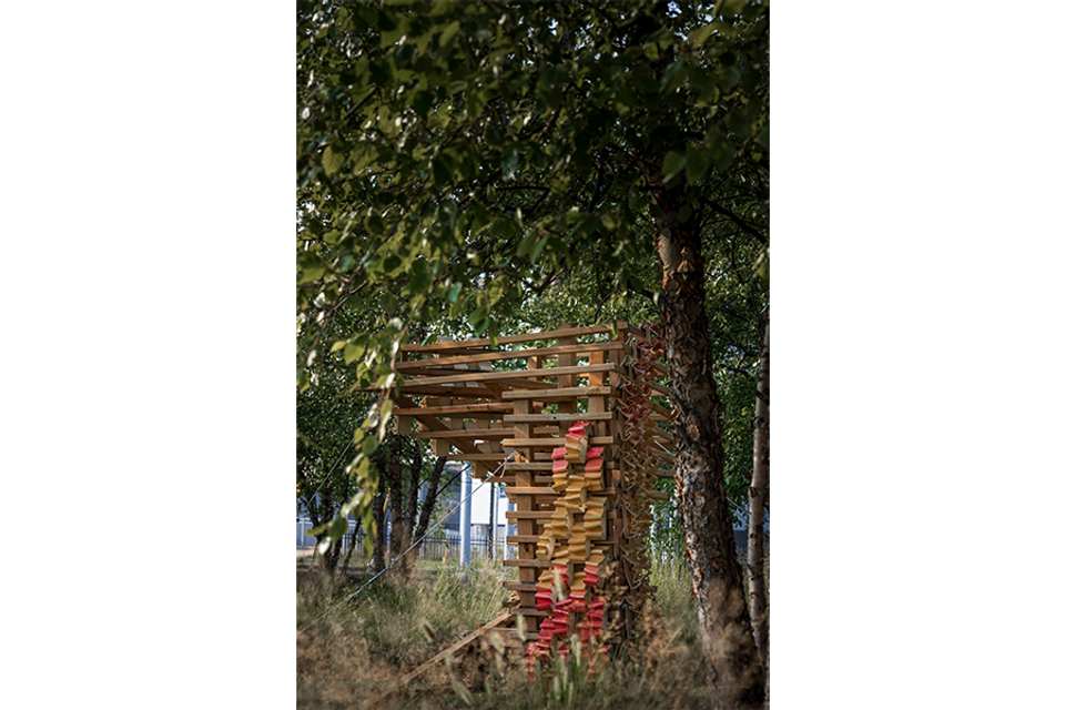 Wood and ceramic sculpture outdoors next to tree and native grasses