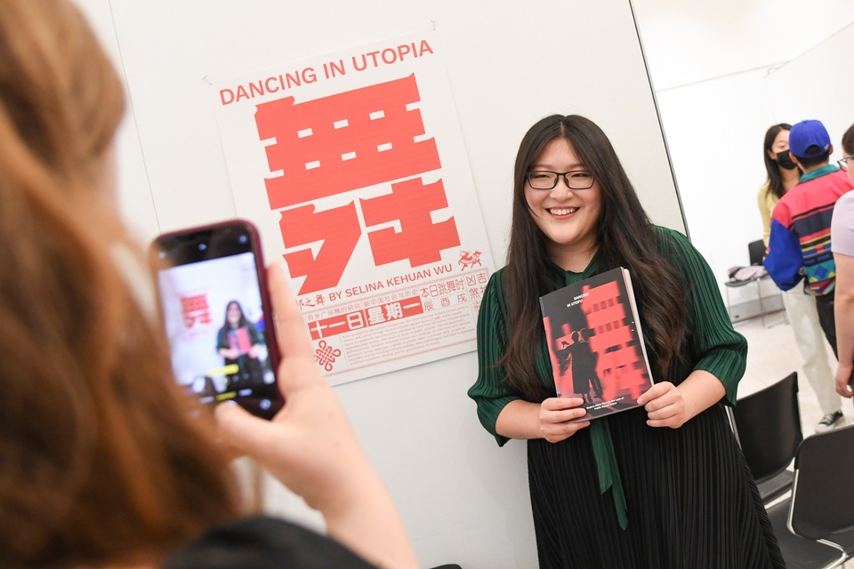 Selina Kehuan Wu poses with her book and poster Dancing in Utopia