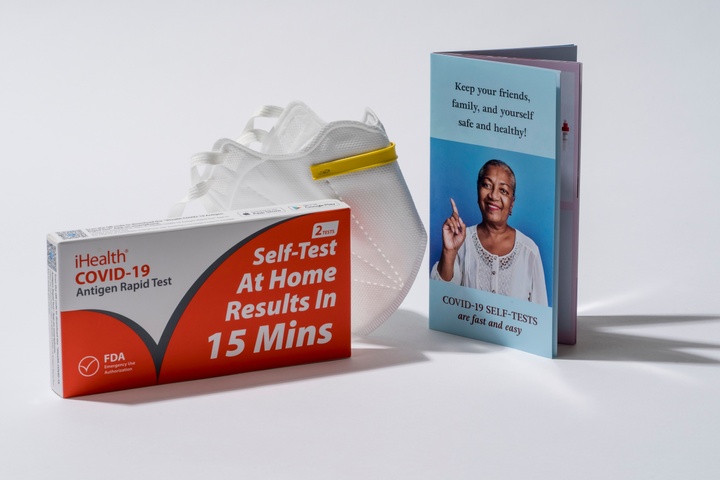 An iHealth test kit next to a white medical mask and instructional booklet.