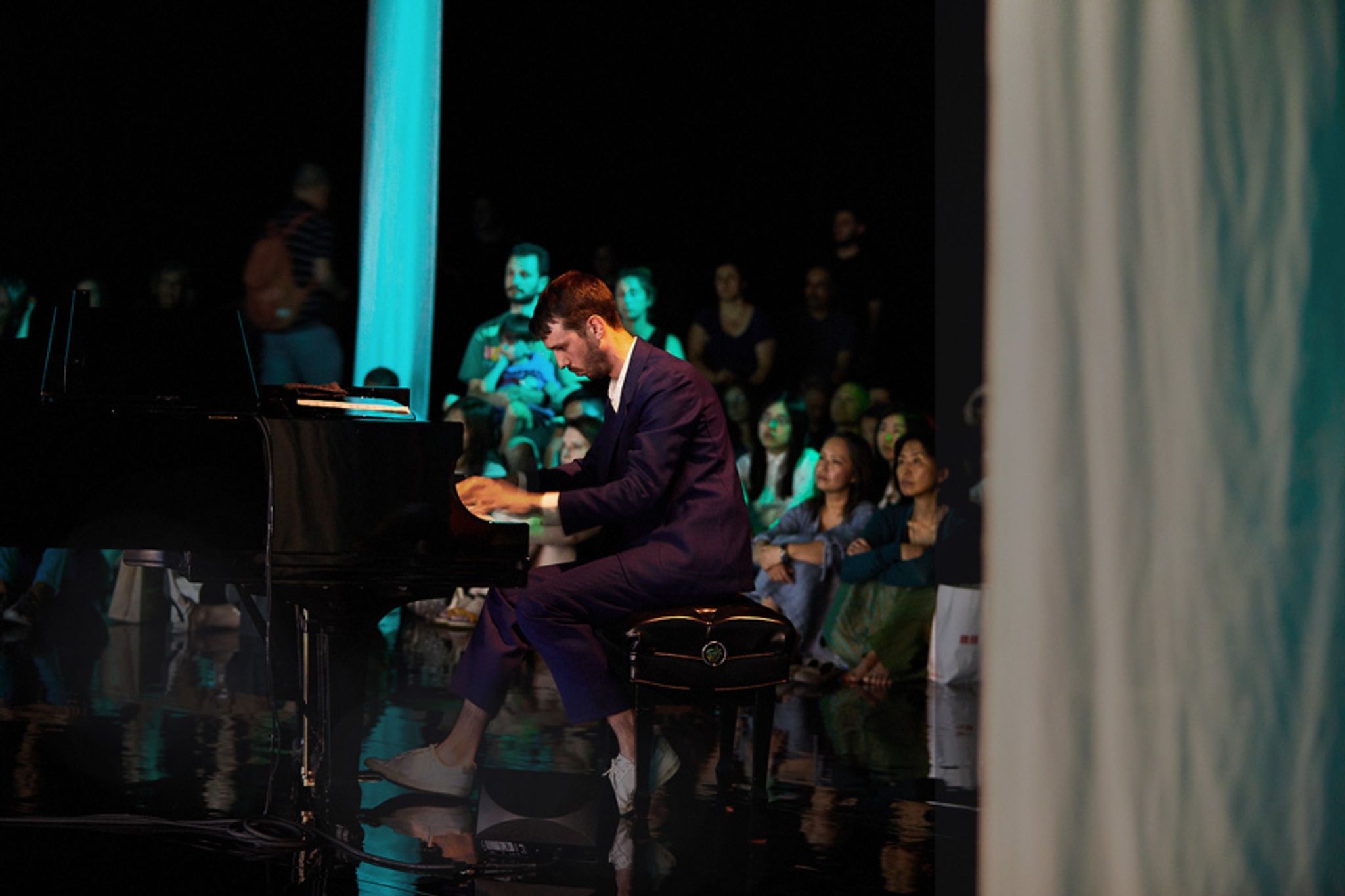 Pianist playing in front of large screens in blue-lit space.