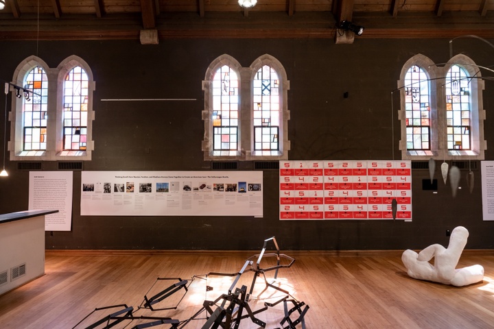 Wall of chapel space with stained glass windows hung with two large design printouts.