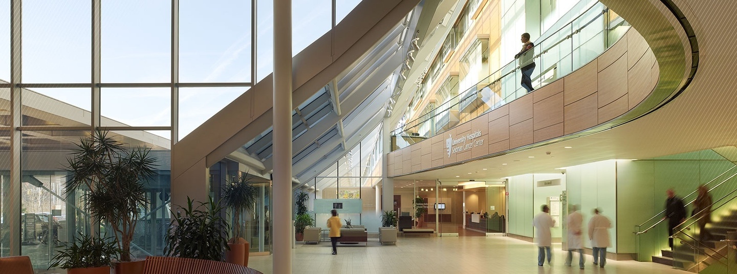 Interior photo of an open two-story atrium area of a cancer hospital, with tall windows in the left portion of the background and a curved architectural element for the second floor.