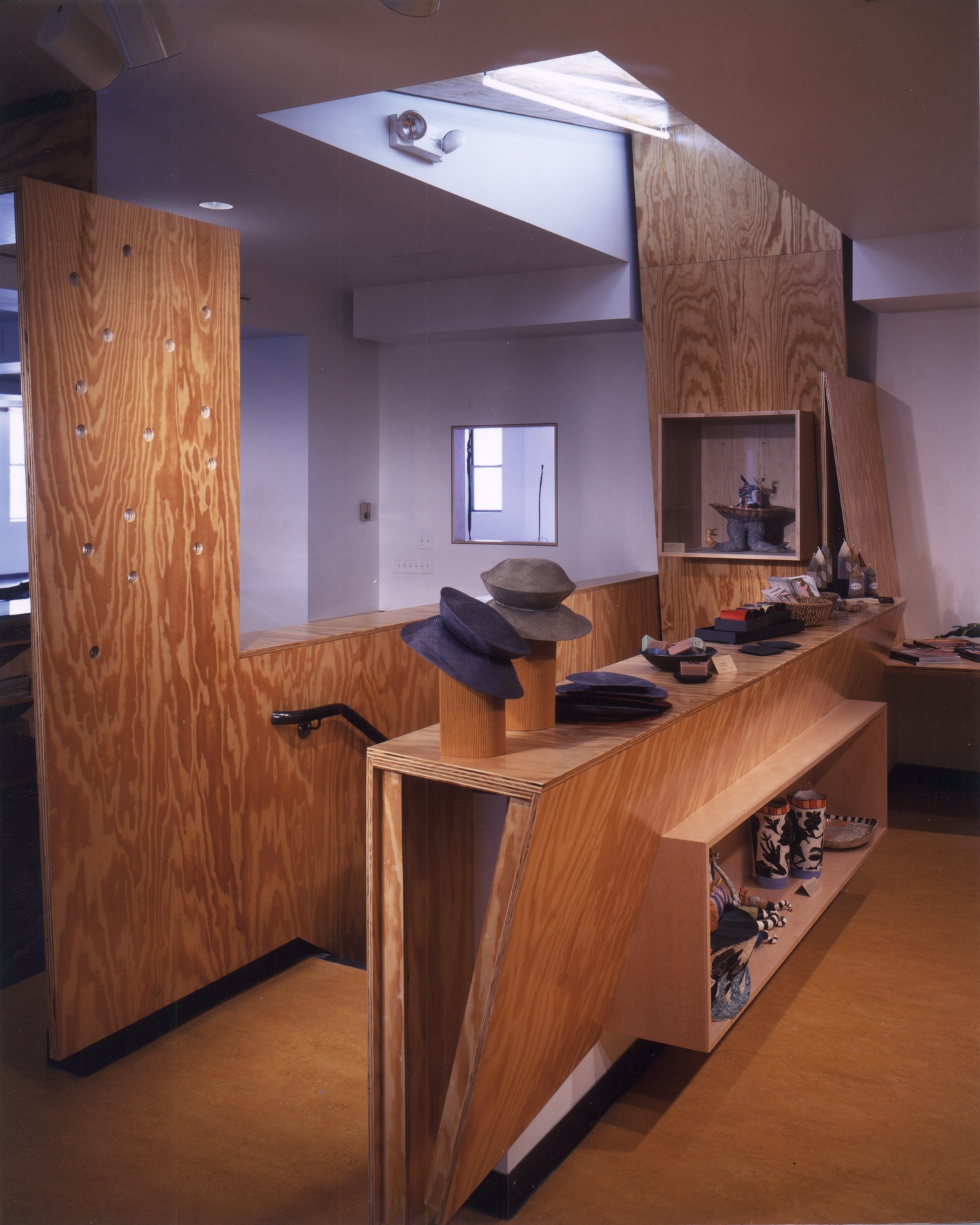 An interior photograph showing a wood and white drywall contrast underneath a skylight which is situated over a stairwell. There is shelving with various hats displayed.