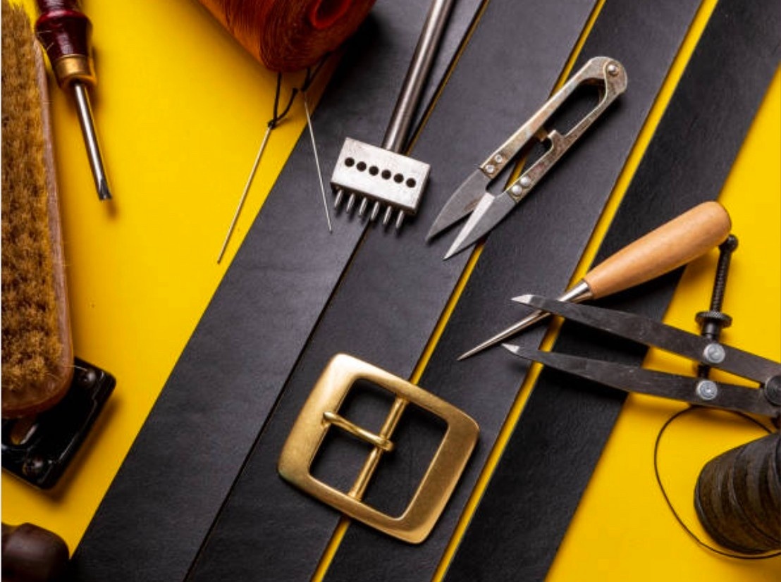 Stylized flat-lay of 4 diagonal strips of leather for belt-making and various related hardware and equipment