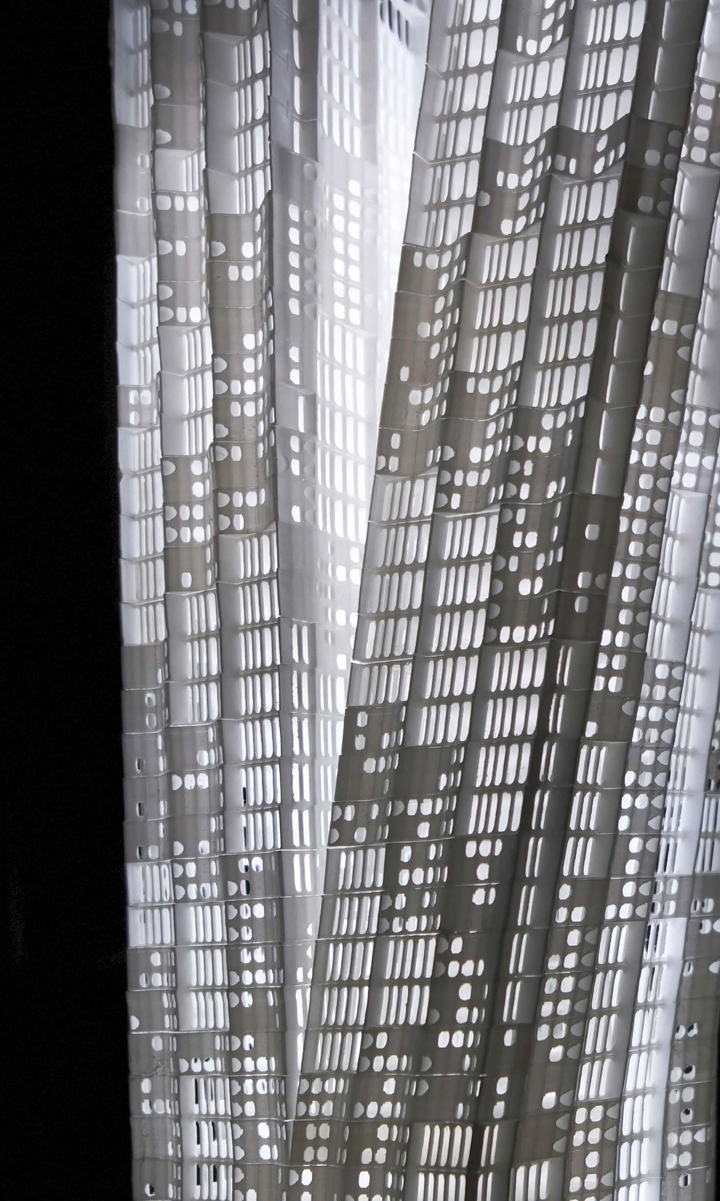 Closeup of a white architectural tall building model lit from within with small round windows as well as long floor to ceiling windows 