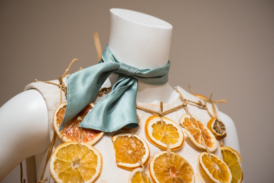 Detail of a mannequin with a teal satin neckscarf and a collar made of dried orange slices strung together.