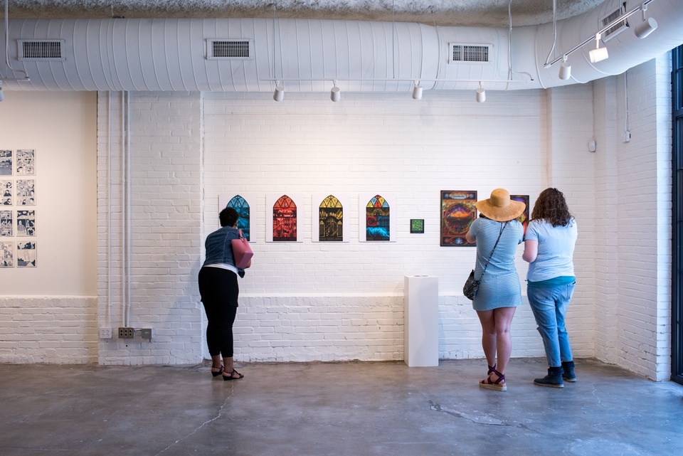 Three people look at a set of prints - four stained glass window designs, and two 3D posters.