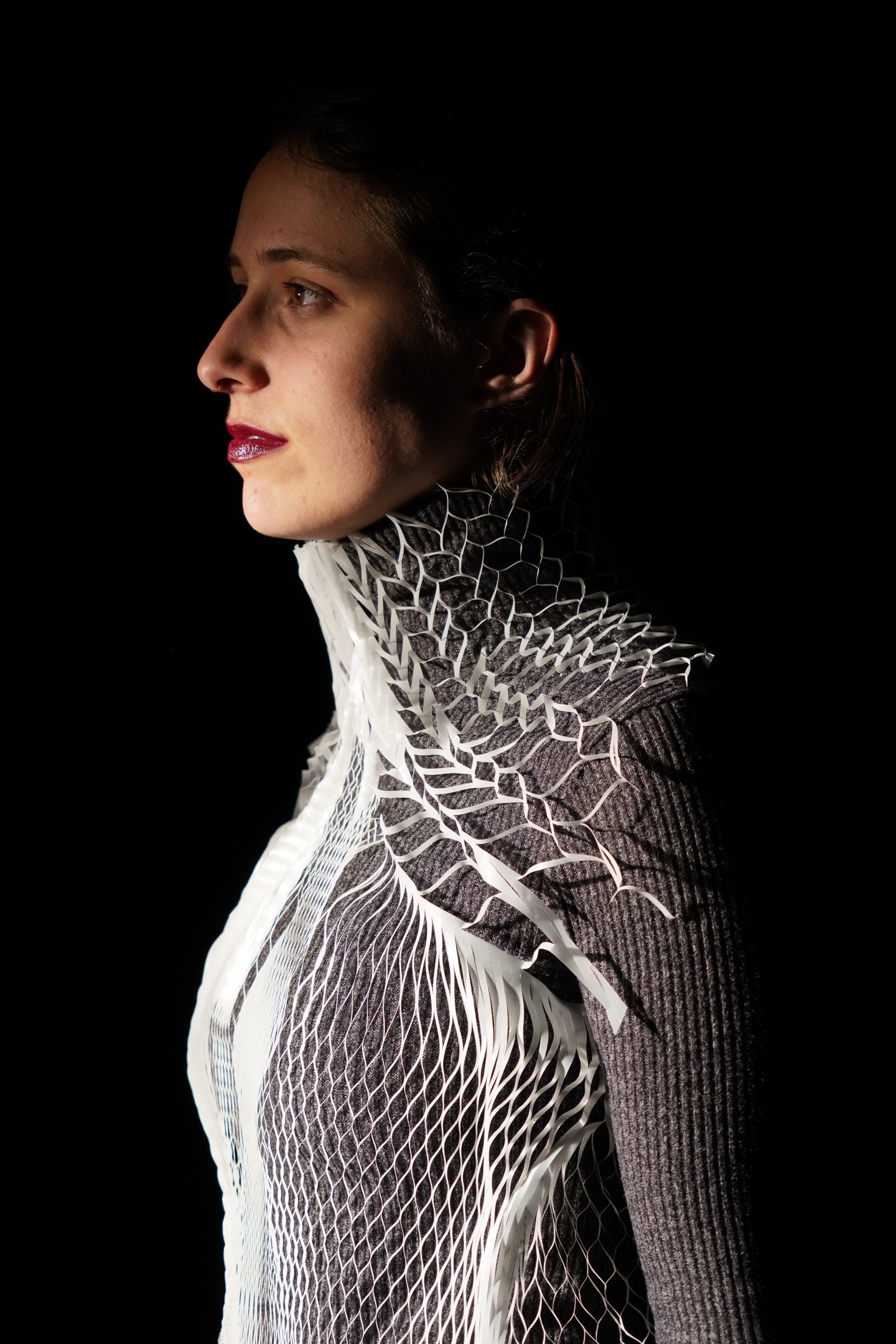 Person's torso in profile wearing a white 3D printed mesh vest with collar over a grey turtleneck.