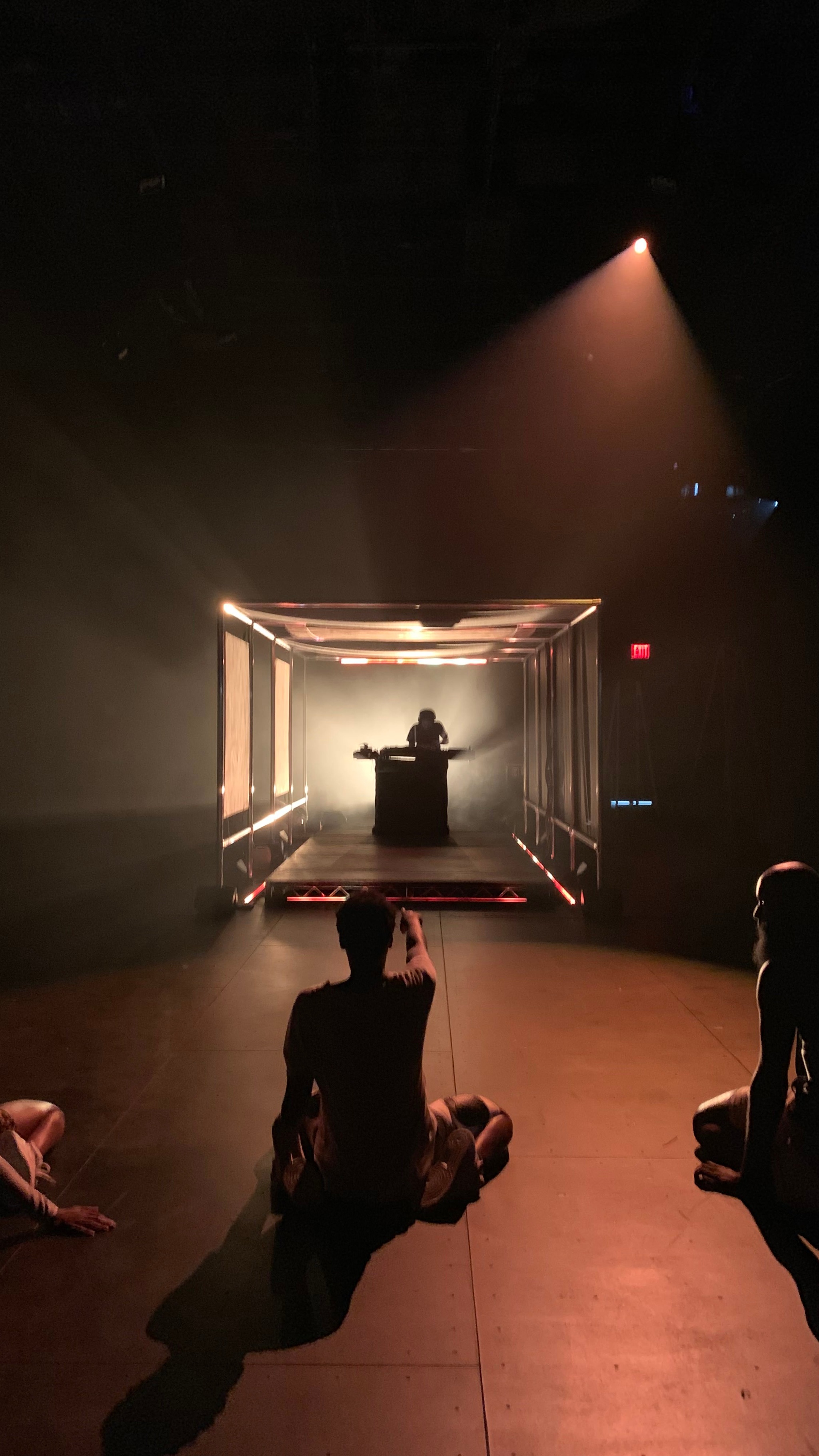 Dancers on a dramatically lit stage with DJ in the background.