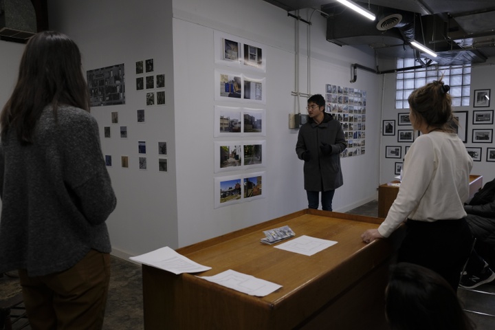 Photograph of three people standing in a gallery with photographs on the walls, having a conversation. 
