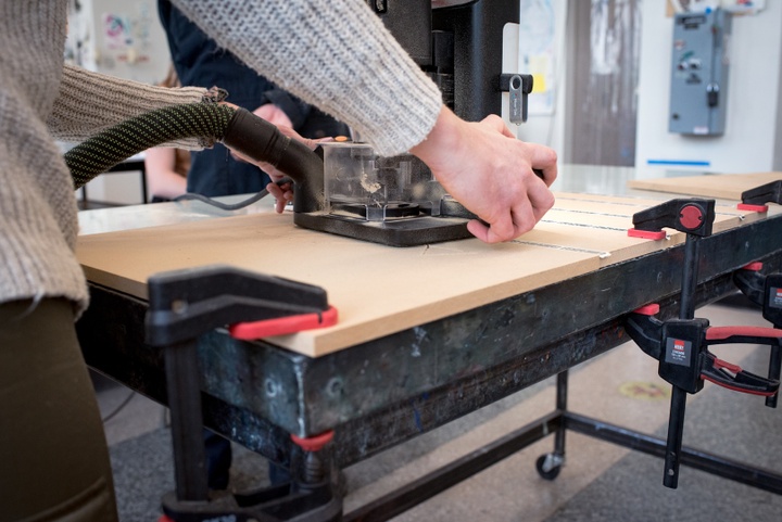 Close up of someone's hands holding the handles of a machine sitting on top of a wood block. Grooves have been cut into the block.