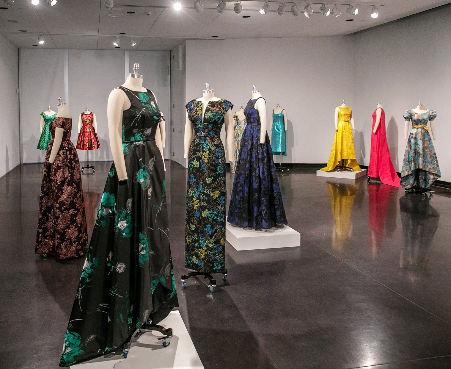 Multiple mannequins wearing colorful gowns placed throughout a room.