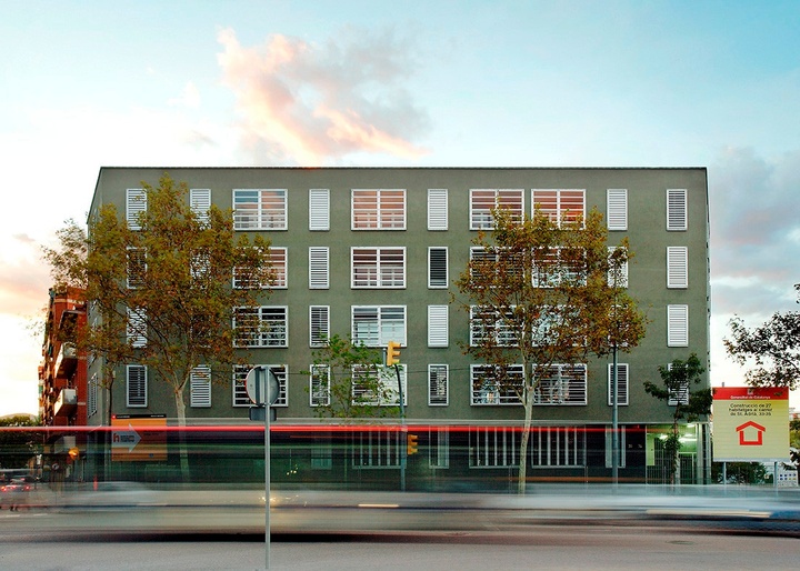Five story, olive-green building with numerous rows of white windows with horizontal blinds.