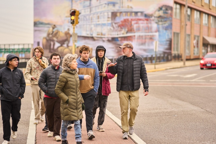 Group of students and faculty walking down the street in Alton, Ill., past a mural of a steamboat.
