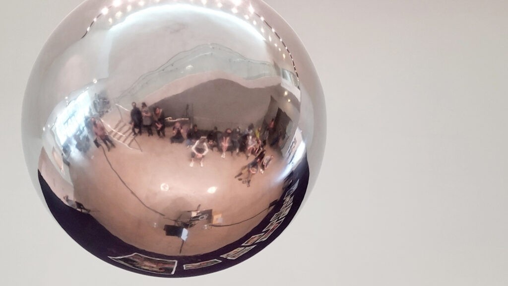 An image of a large reflective chrome ball with an image of students in the Kemper museum reflected on it