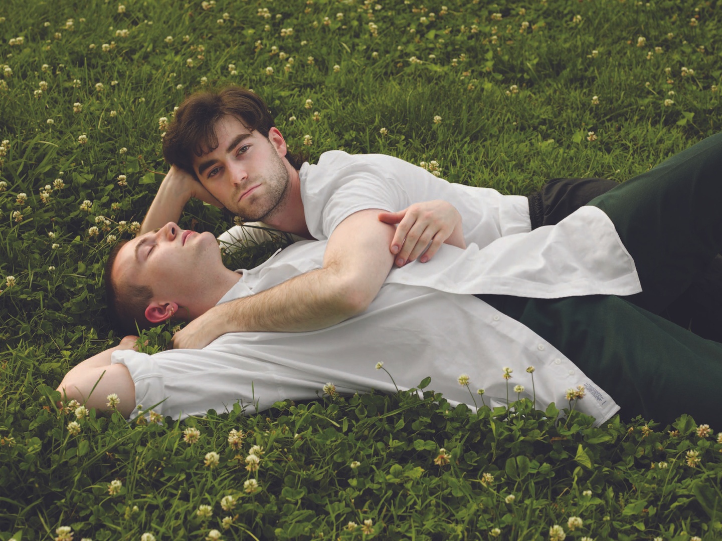 Two figures dressed in white shirts lie in each other's arms on the grass