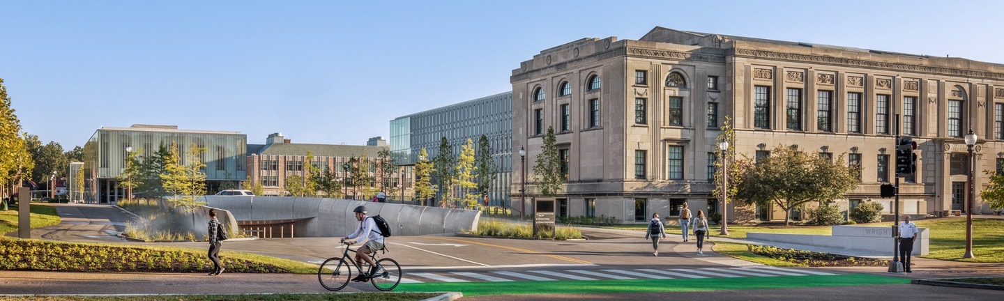An exterior view of WashU campus buildings with people walking and riding bikes.