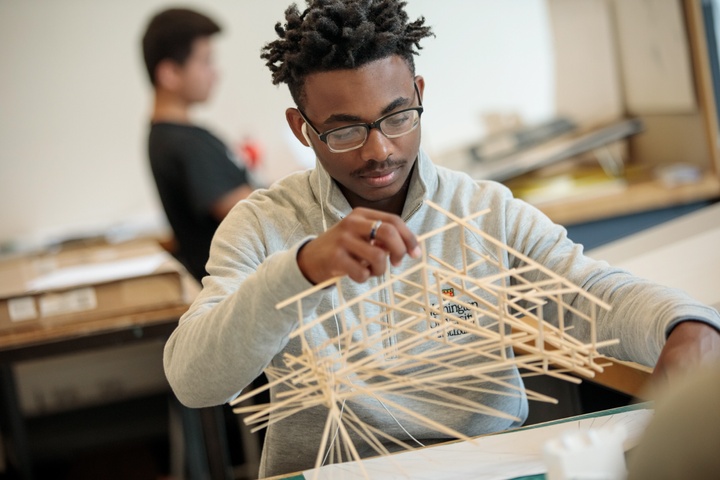 A person works on an elaborate architectural model of wooden sticks.