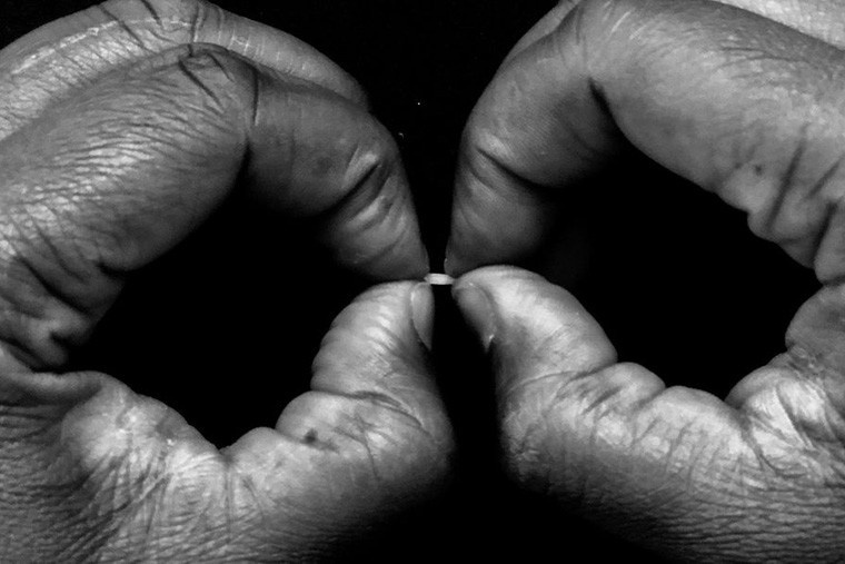 Close-up black and white photo of a pair of hands, thumbs and forefingers coming together in a circule to hold a tiny grain of rice.