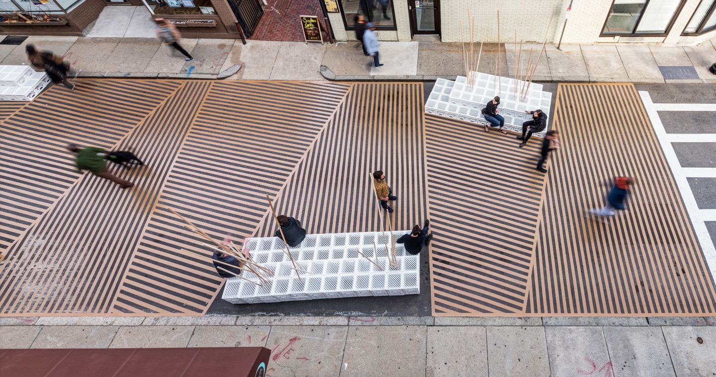 Birds eye view of a plaza with parallel stripes going different directions and white bottle crate-like seats arranged side by side each other