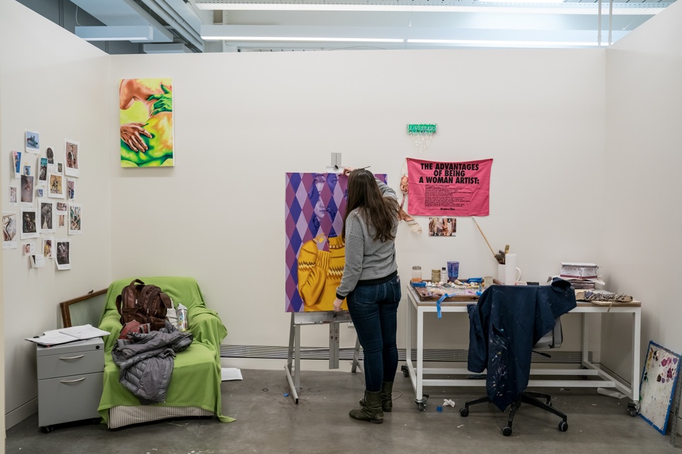 Private studio space containing a desk, an armchair, a file cabinet, and an easel at which someone is painting.