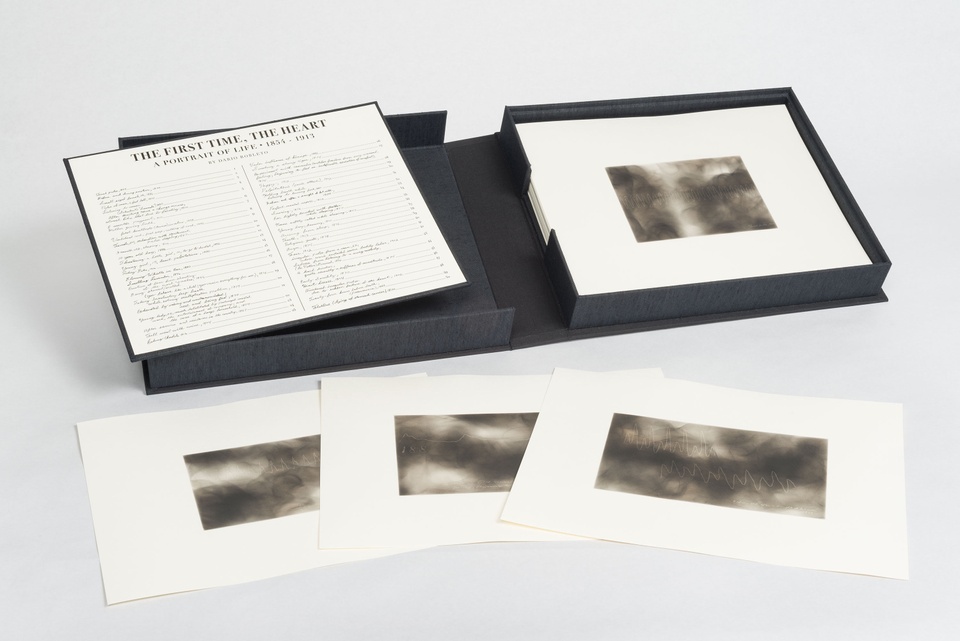 Image of a black portfolio box of 50 photolithographic prints. The images on the individual prints are gray and smokey with cardiogram-like lines