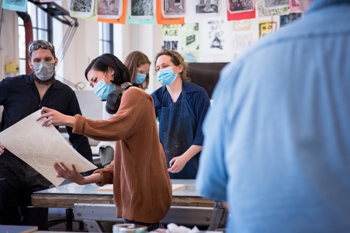 Person admires a print pulled off a printmaking press and holds it up for others to see.