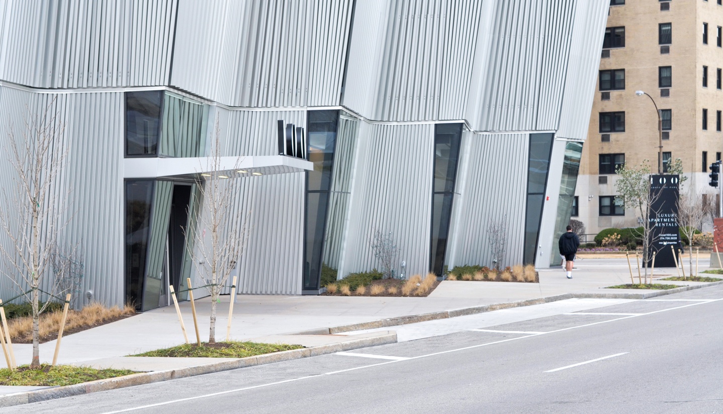 Young trees and bushes in diamond-shaped beds along the exterior of a modern high-rise apartment complex.