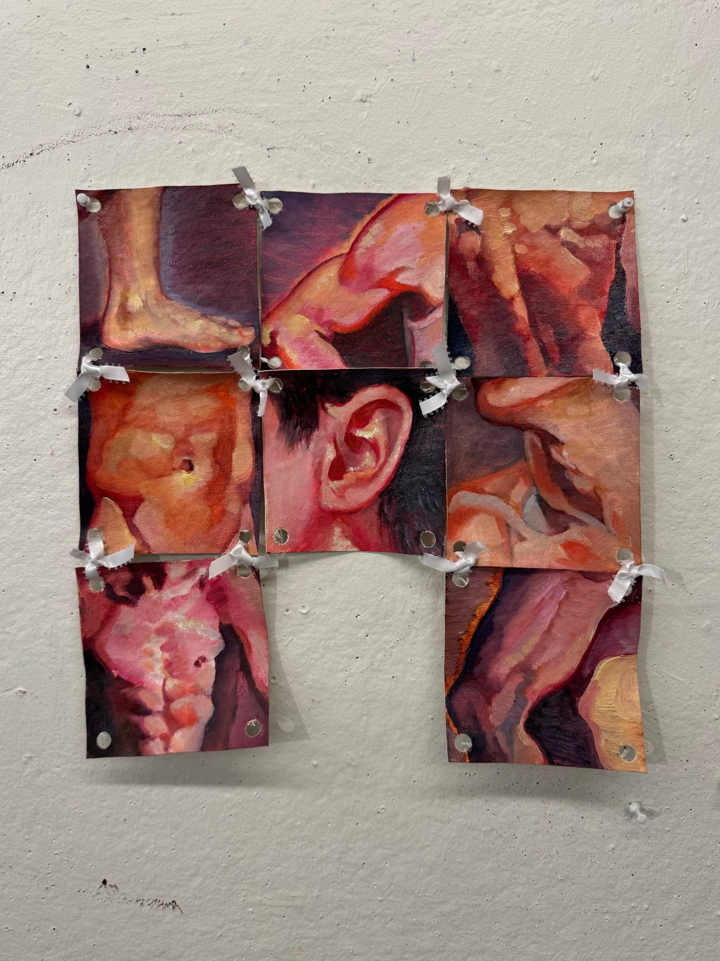 A collage of small square paintings of body parts, attached at the corners through holes with tied gray ribbon.