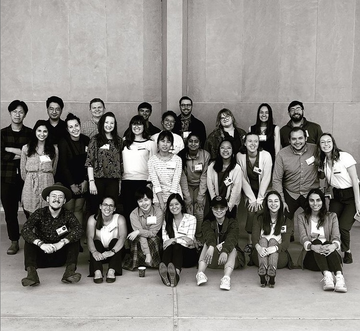 Black and white photo of many students in three rows posing for the camera against a concrete wall.