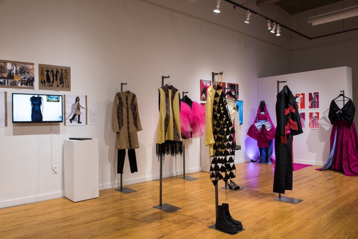 Closer view of three garments in a collection. One is a dress sheath made from black plastic triangles linked together; the second is a yellow princess cut minidress with black fringe; the third is a beige thigh-length coat over black leggings.