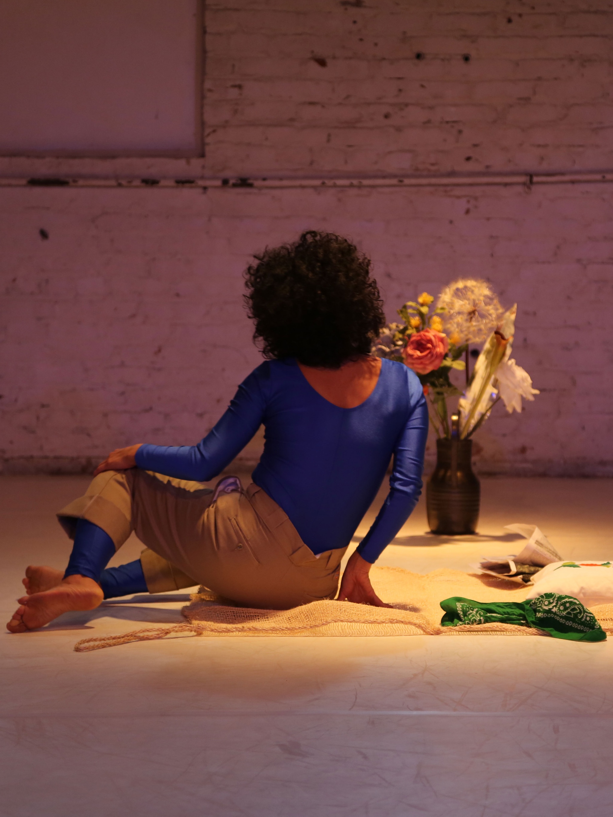 Woman sitting on the floor near bouquet of flowers in vase.