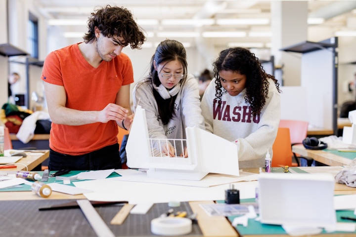 Three students work on a white foamcore shadowbox in an architecture studio.