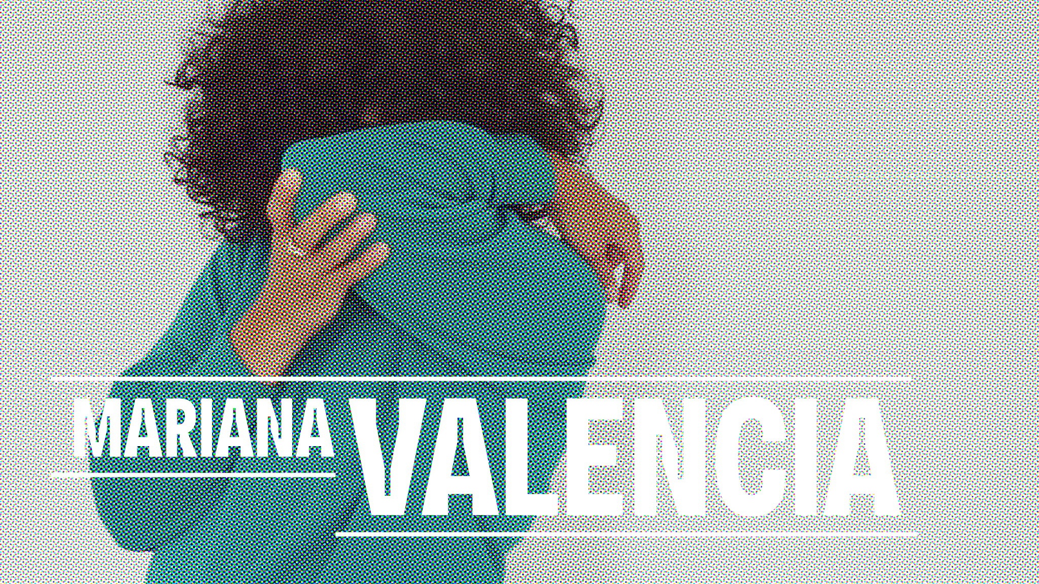 A photo of artist Mariana Valencia in a teal sweatshirt hiding their face behind their arm and elbow with the name Mariana Valencia superimposed in white type