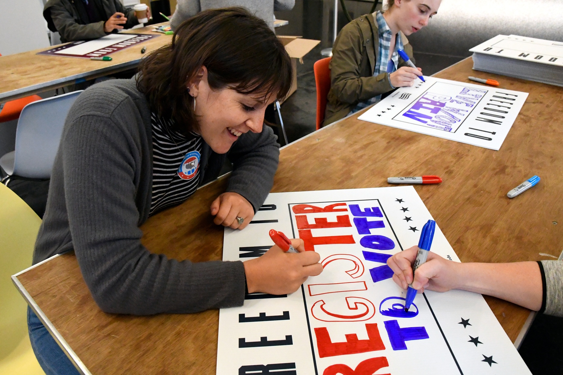 Two light-skinned people working on a sign with "Freedom to Register to Vote" written on it.