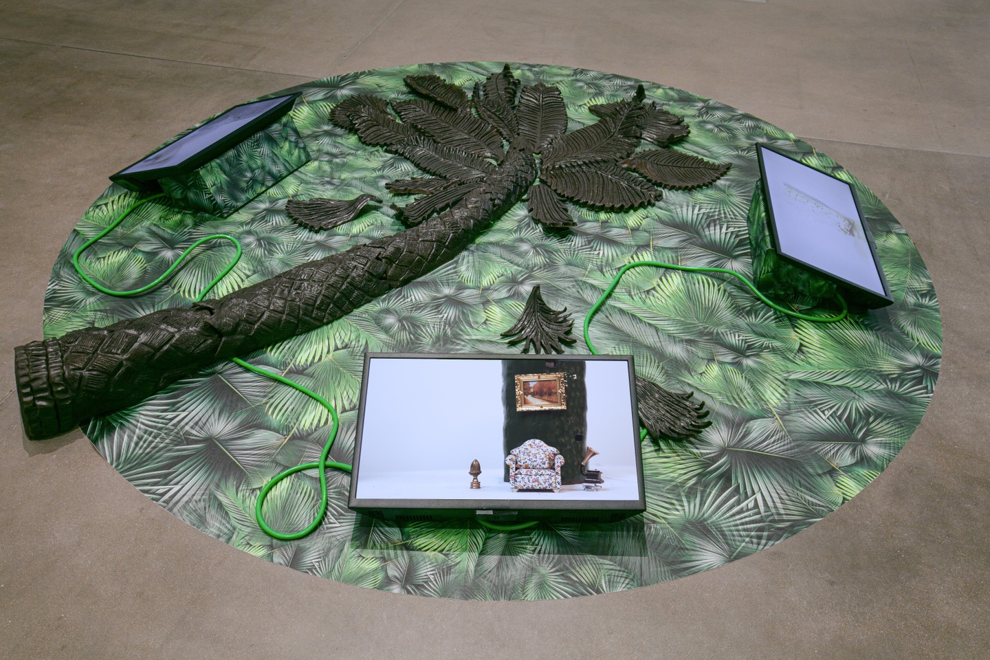 ceramic palm tree laying on the floor on top of a green leaf pattern circle of fabric with three tablets, one shows the image of a dollhouse living room