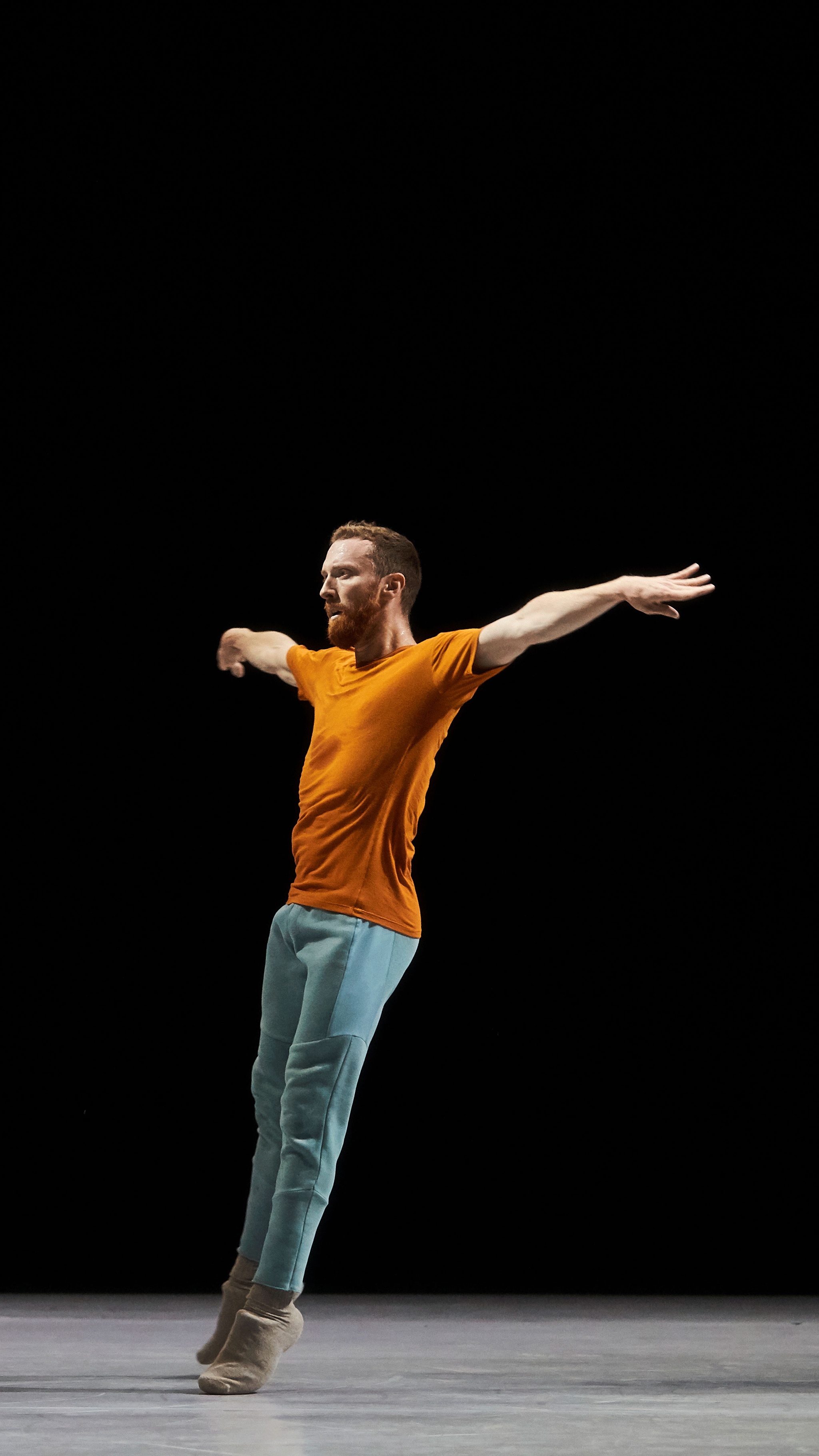Dancer in an orange shirt, dancing against black background.