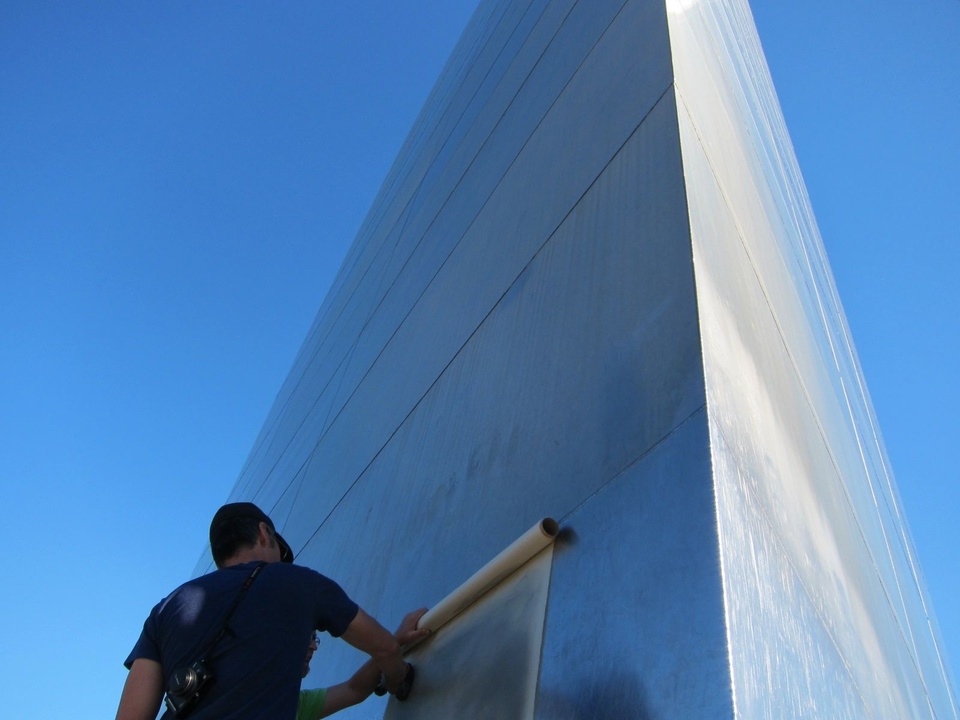 Shaun placing a large sheet of paper flat by the side of a building while rubbing a bunched up cloth over it