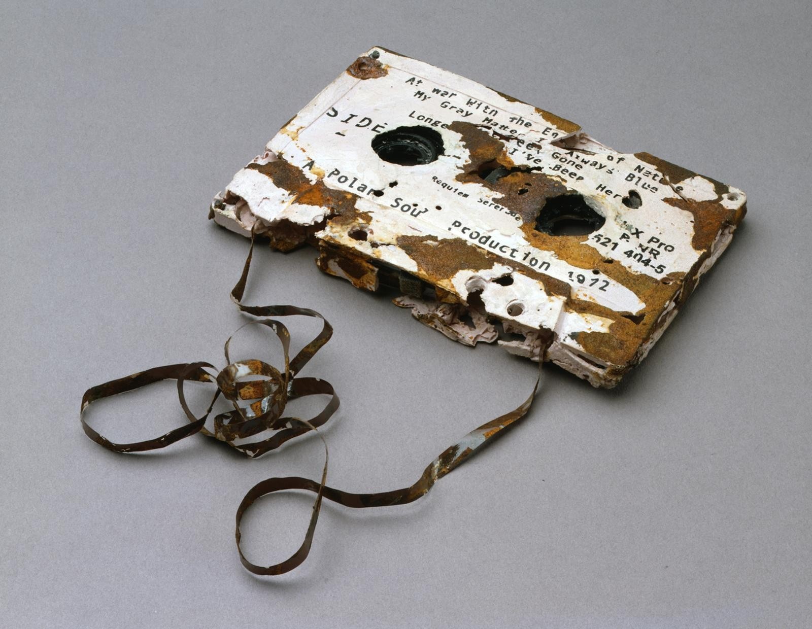 A sculpture of an old, white, rusty cassette tape with some film pulled out and piled next to it.